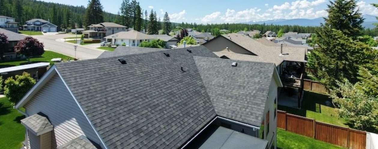 Aerial view of a home with grey asphalt shingle roofing in a East Kootenay neighbourhood.